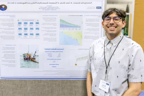 A student stands in front of their research poster titled, "Farming the Oceans: A Case Study of Seaweed Aquaculture Policy and Regulation in the U.S.”